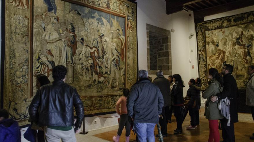 Grupo de personas adultas en una visita guiada en el castillo frente a un tapiz Barroco