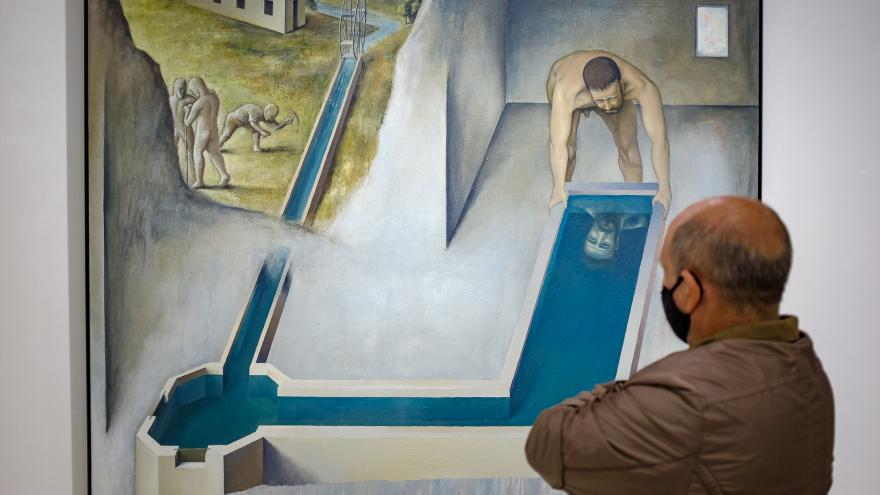 Hombre adulto con mascarilla observando un cuadro donde aparecen unos bañitas