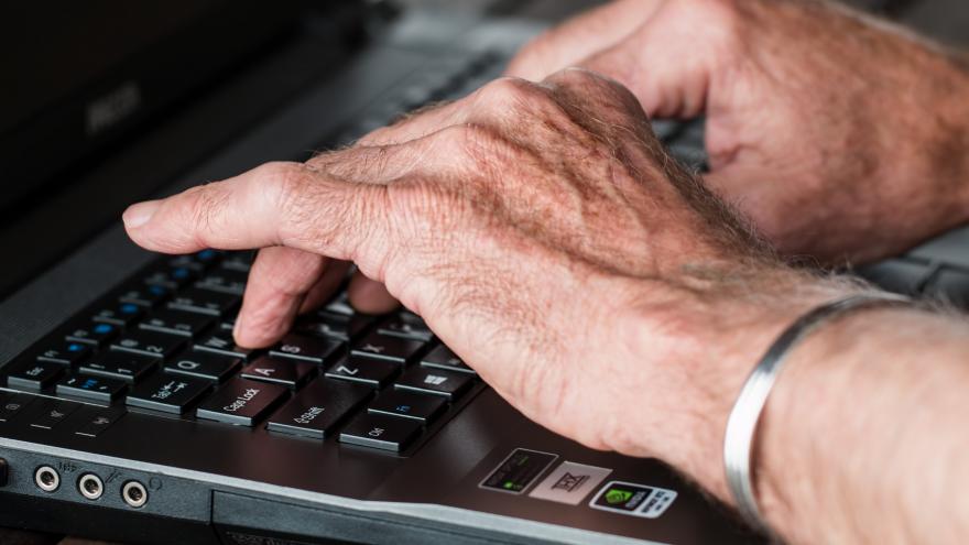 Primer plano de las manos de un hombre mayor sobre teclado de ordenador portátil