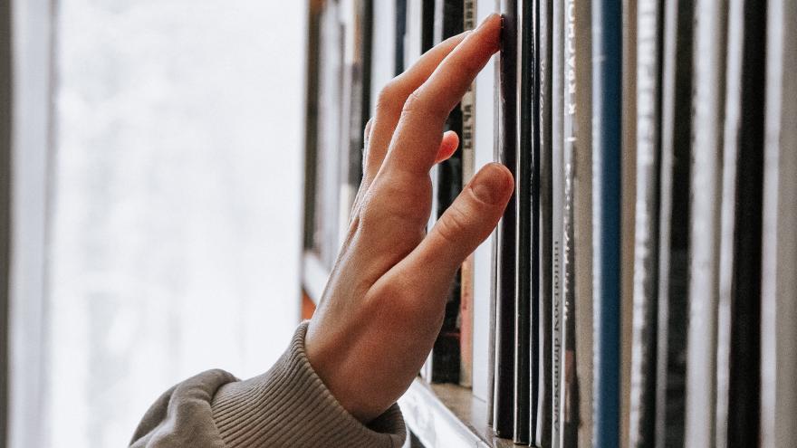 Una mano tocando los libros de una estantería