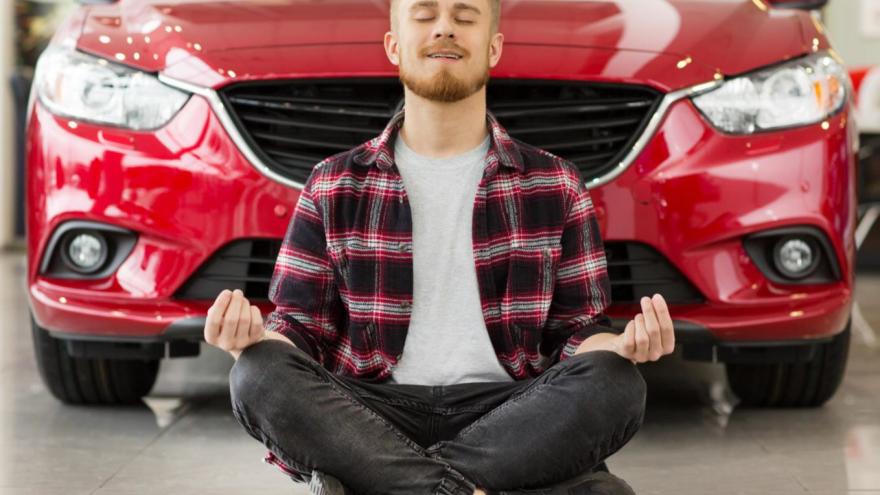 Señor meditando sentado delante de un vehículo rojo