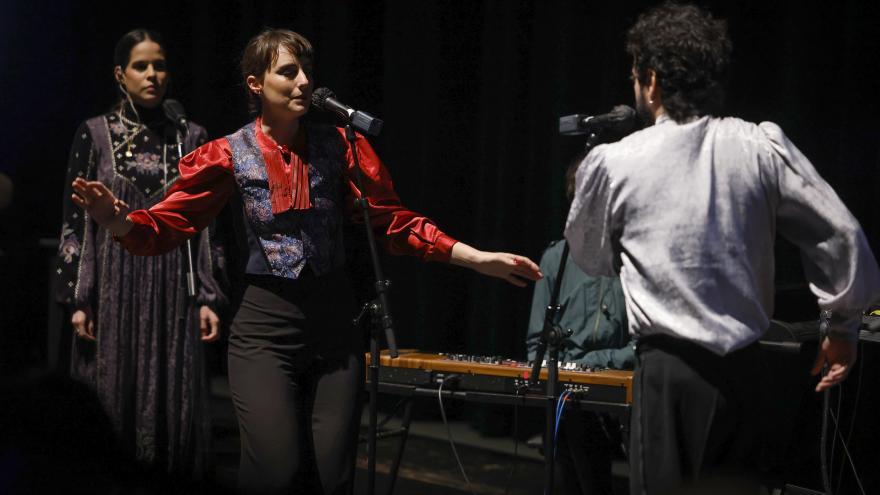 Una mujer canta con los ojos cerrados y se observa un hombre 