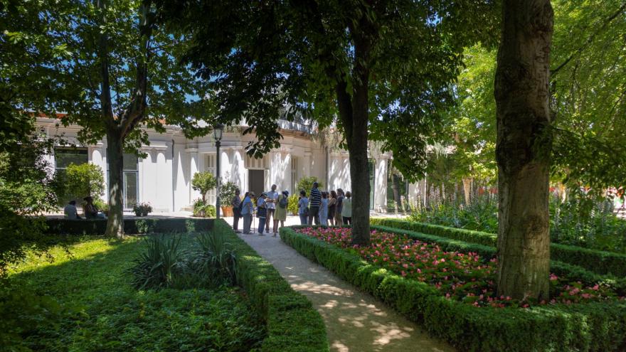 grupo de personas de espaldas en una visita guiada en un jardín con edificio al fondo