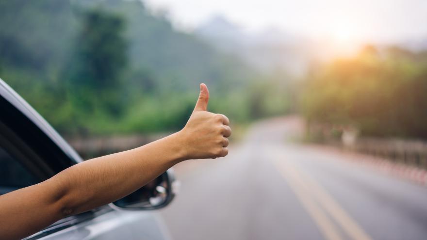 imagen de mano cerrada con pulgar arrriba en coche en marcha por carretera