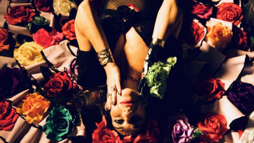 fotografía de una mujer caracterizad como Frida Kahlo, con flores en el pelo, tumbada en un lecho de flores de muchos colores 