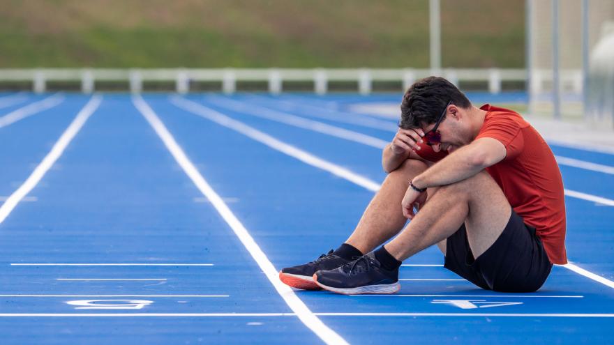 Corredor exhausto con cara de sufrimiento se sienta en el suelo en la línea de meta de una pista de atletismo