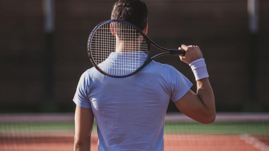 Tenista de espaldas sujetando la raqueta por encima del hombro