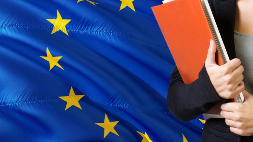 Joven con carpetas  delante de una bandera de la UE