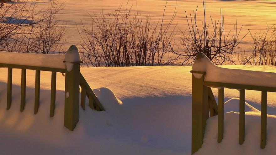 Paisaje nevado al atardecer, con una valla en primer, un campo lleno de nieve y árboles
