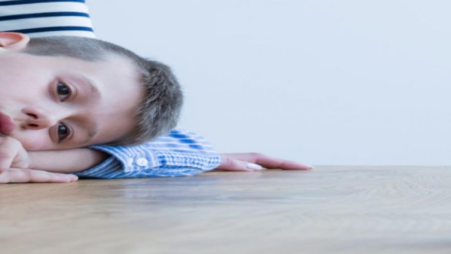 Foto de niño autista acostado sobre una mesa con mirada perdida.