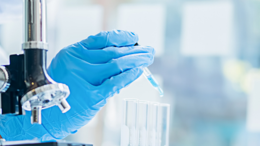 torso de mujer visto de lado a la izquierda con bata blanca y pipeta en la mano en laboratorio