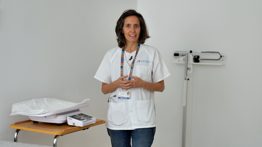doctora con pijama blanco y vaqueros posando al lado de máquina de pesar bebés
