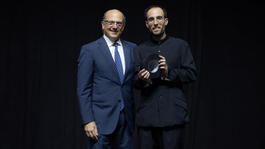 hombre con traje azul oscuro recibiendo un premio sobre un fondo azul oscuro