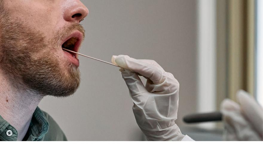 Manos con guantes cogiendo muestra saliva de la boca de un varón