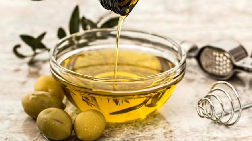 Botella de aceite de oliva rellenando un cuenco y unas aceitunas de adorno