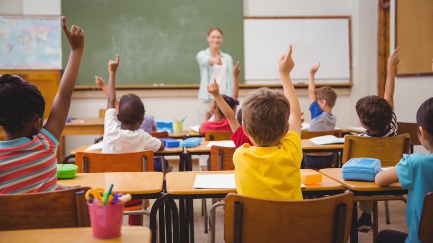 Un salón de clases con varios alumnos levantando la mano 