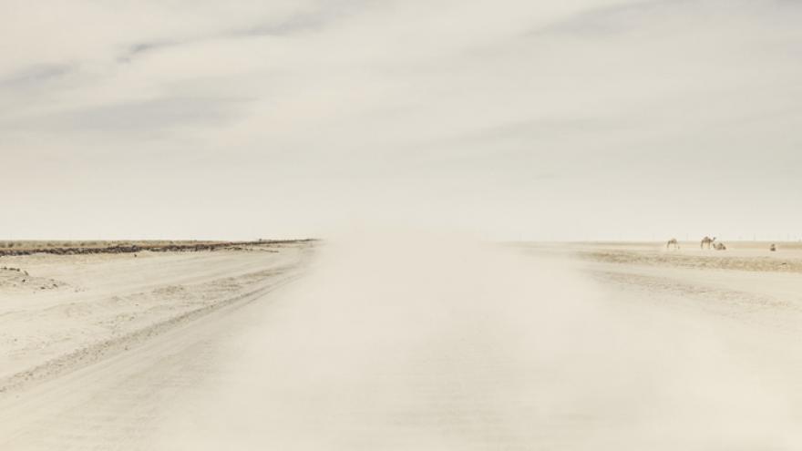 Fotografía con colores cálidos que muestras una carretera desértica y llena de polvo en suspensión