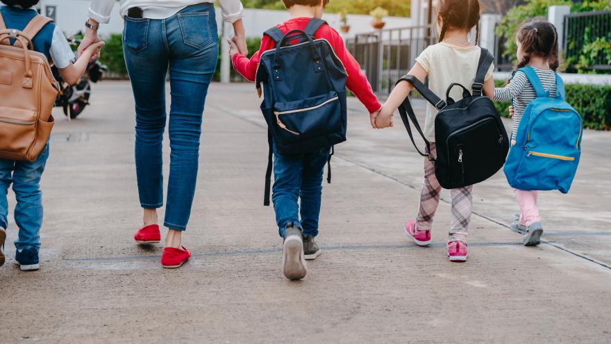 Unos niños llegan a una escuela de la mano de una mujer