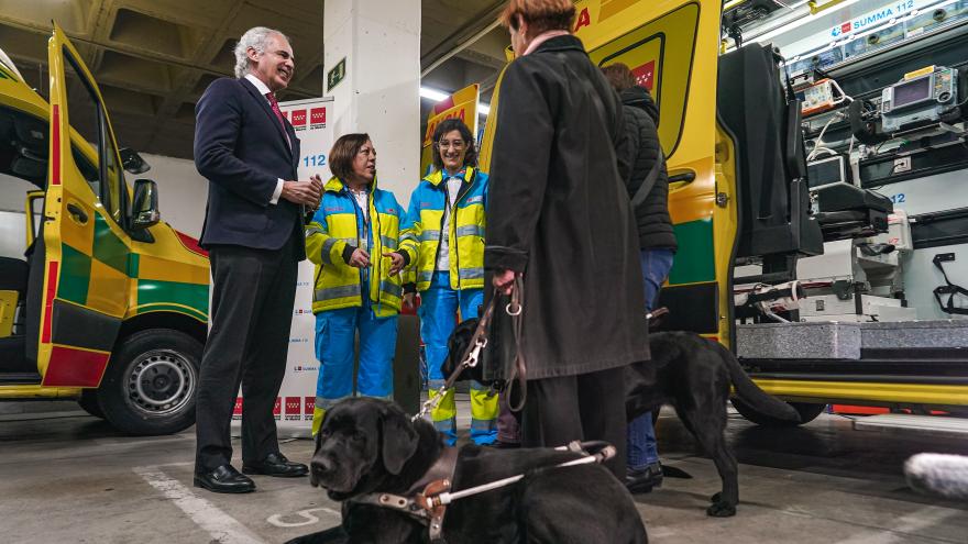 El consejero Enrique Ruiz Escudero conversa con los sanitarios y dos perros de acompañamiento están acostados cerca de él