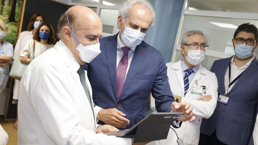 El consejero Enrique Ruiz Escudero observa una tablet mientras habla con un médico