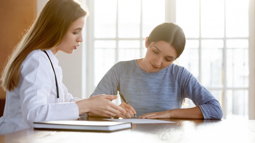 Una mujer firma un papel, junto a una tutora