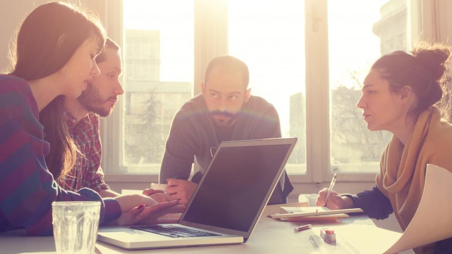People sitting around a table, where there is a laptop, during a business meeting.