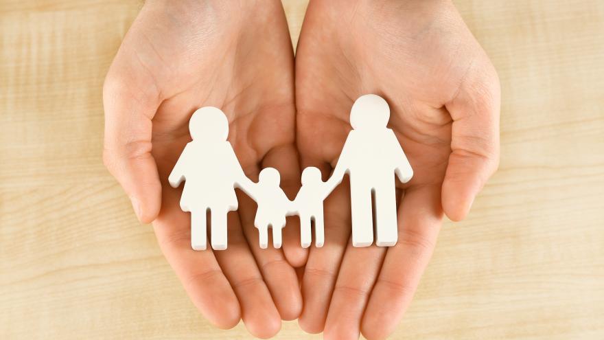 Unas manos sujetan unas figuras de papel representando a una familia