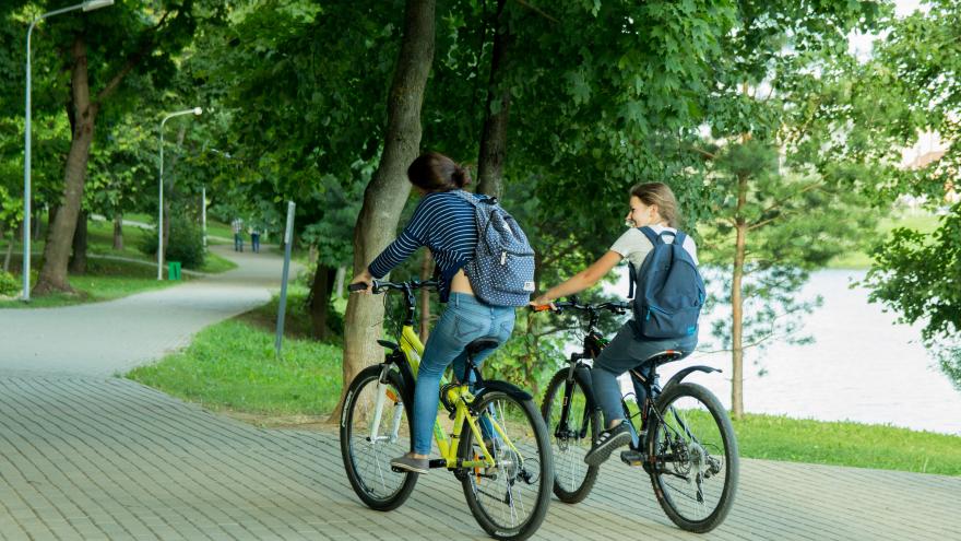 Dos chicas en bici por zona ajardinada