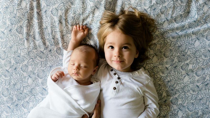 Bebé con su hermana encima de una cama Bebé con su hermana encima de una cama