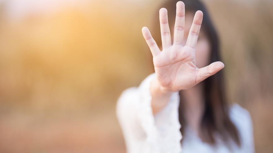 Mujer con el brazo estirado y la palma de la mano abierta tapando su cara