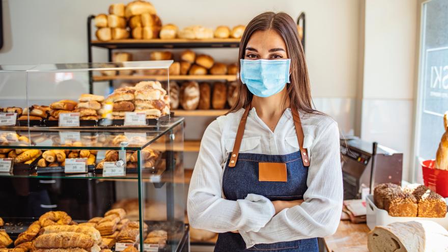 Mujer con mascarilla y delantal atendiendo una panaderia