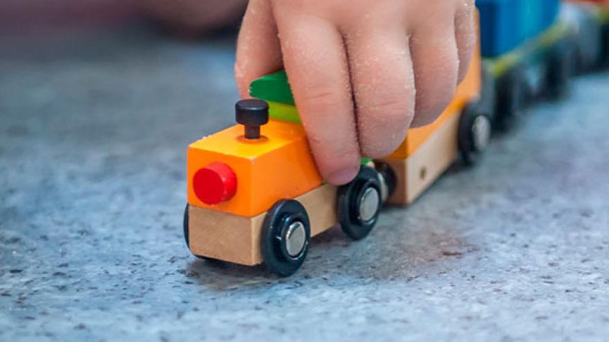 Detalle de la mano de un bebé que juega con un tren de madera