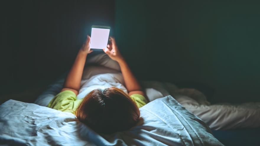 Chica tumbada en la cama mirando un teléfono