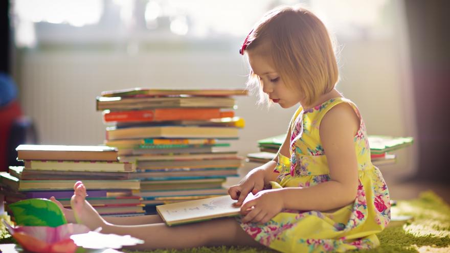 Niña sentada en el suelo con una pila de libros, leyendo