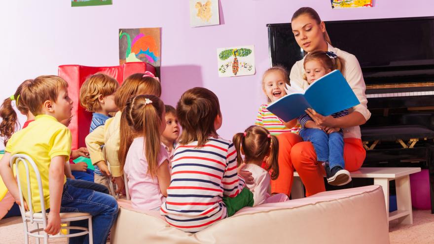Niños en una clase de educación infantil sentado en el suelo alrededor de la profesora que está leyendo un libro