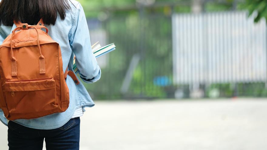 Chica joven caminando con una mochila a su espalda y libros en las manos