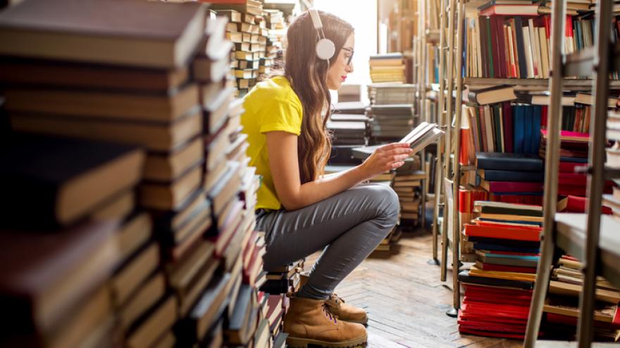 Chica de pelo largo y con gafas sentada entre pilas de libros