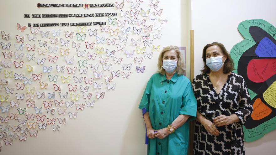 La consejera junto con otra mujer posan delante de un  mural con mariposas de papel pegadas