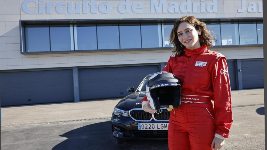 La presidenta con el casco en la mano y mono de piloto posando ante un coche