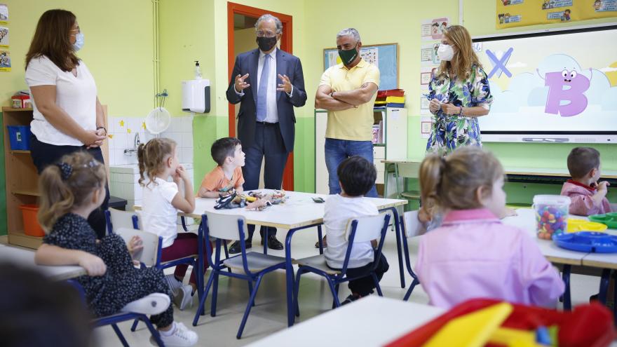 Enrique Ossorio acompañado de miembros del colegio en una clase hablando con alumnos sentados en sus pupitres