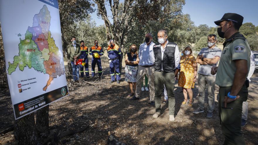 El consejero junto a más personas en el bosque observando un mapa de la Comunidad de Madrid y atendiendo a la explicación de un agente forestar