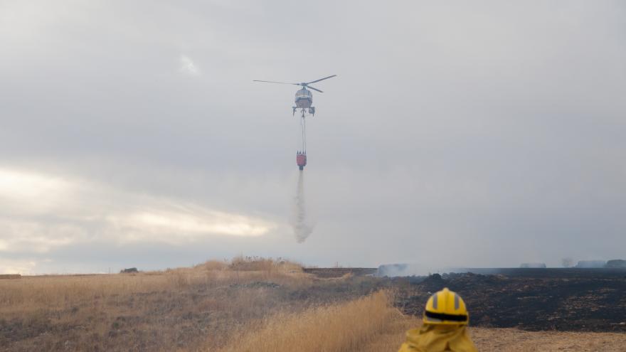 Un bombero de la Comunidad de Madrid y un helicoptero volando en el cielo mientras suelta agua