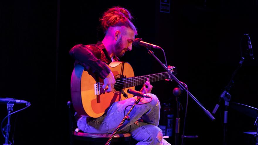 Hombre sentado tocando la guitarra sobre fondo negro