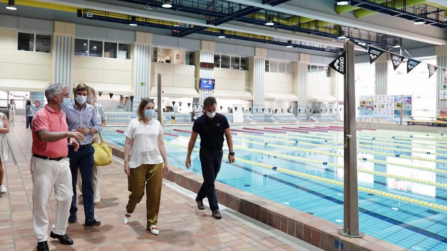 La consejera caminando al lado de una piscina mientras escucha la explicación de unos de los responsables de las instalaciones