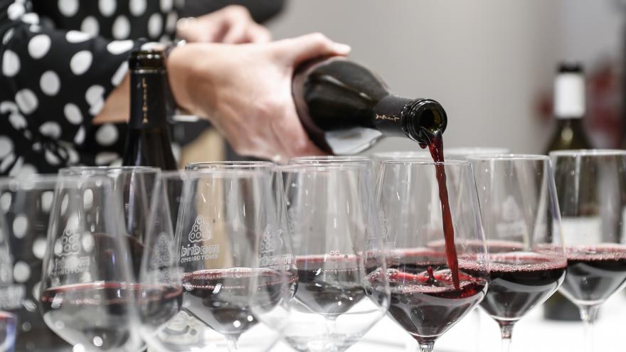 Las manos de una persona sirviendo varias copas de vino tinto