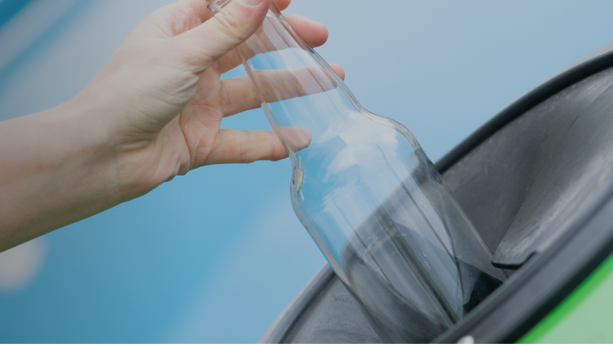 Fotografía de una mano echando una botella de vidrio al contenedor de reciclaje de vidrio