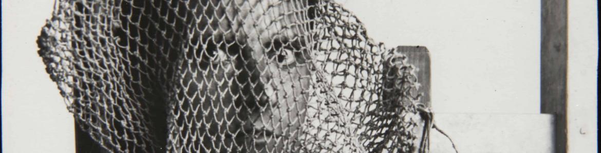 Fotografía en blanco y negro de una cabeza de hombre dentro de una red de pesca