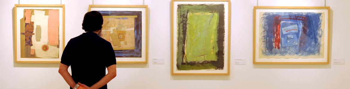 Hombre de pie observando varios cuadros abstractos de colores en la pared de una exposición