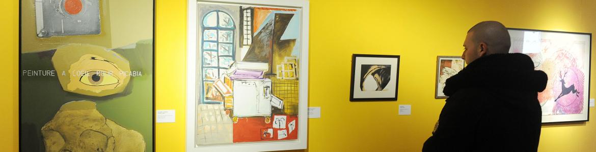 Hombre mirando obras de arte en una exposición con paredes amarillas