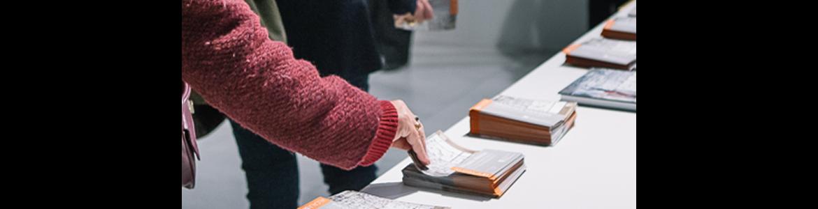 Mano cogiendo un folleto en una mesa blanca en un museo